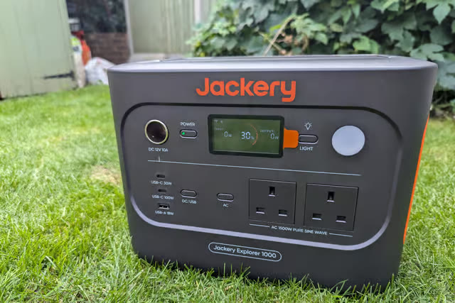 Jackery Explorer 1000 v2 portable power station on a lawn, showing its two UK mains sockets, USB ports and charge display